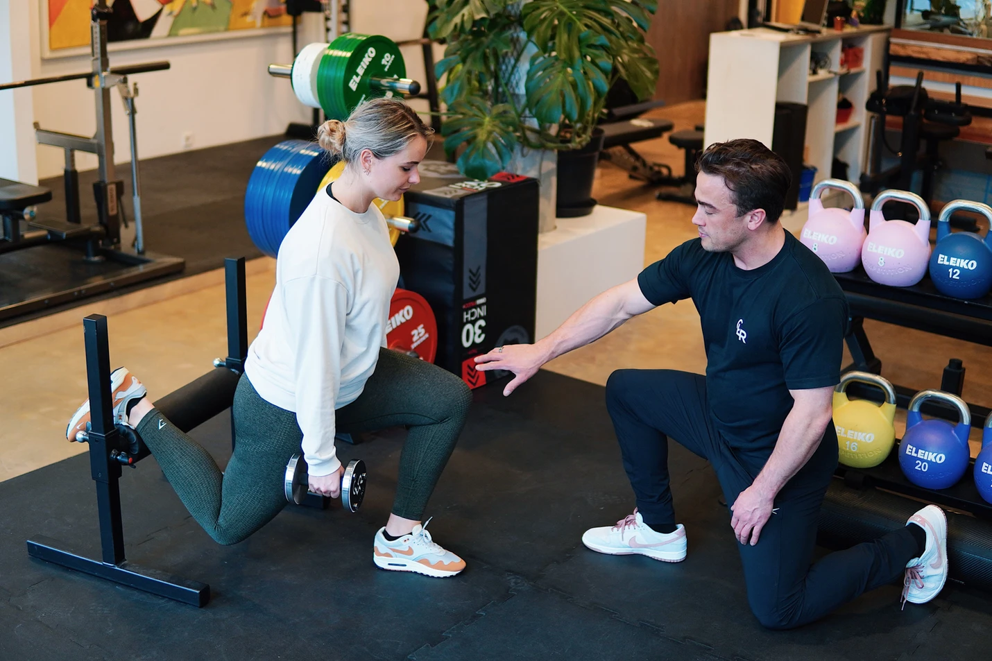 Image of a trainer helping a client train client is doing a split squat where 1 leg is elevated